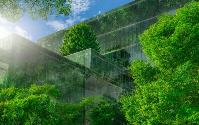 Selective focus on tree and eco friendly building with vertical garden in modern city. Green tree forest on sustainable glass building. Office building with green environment. Go green concept.